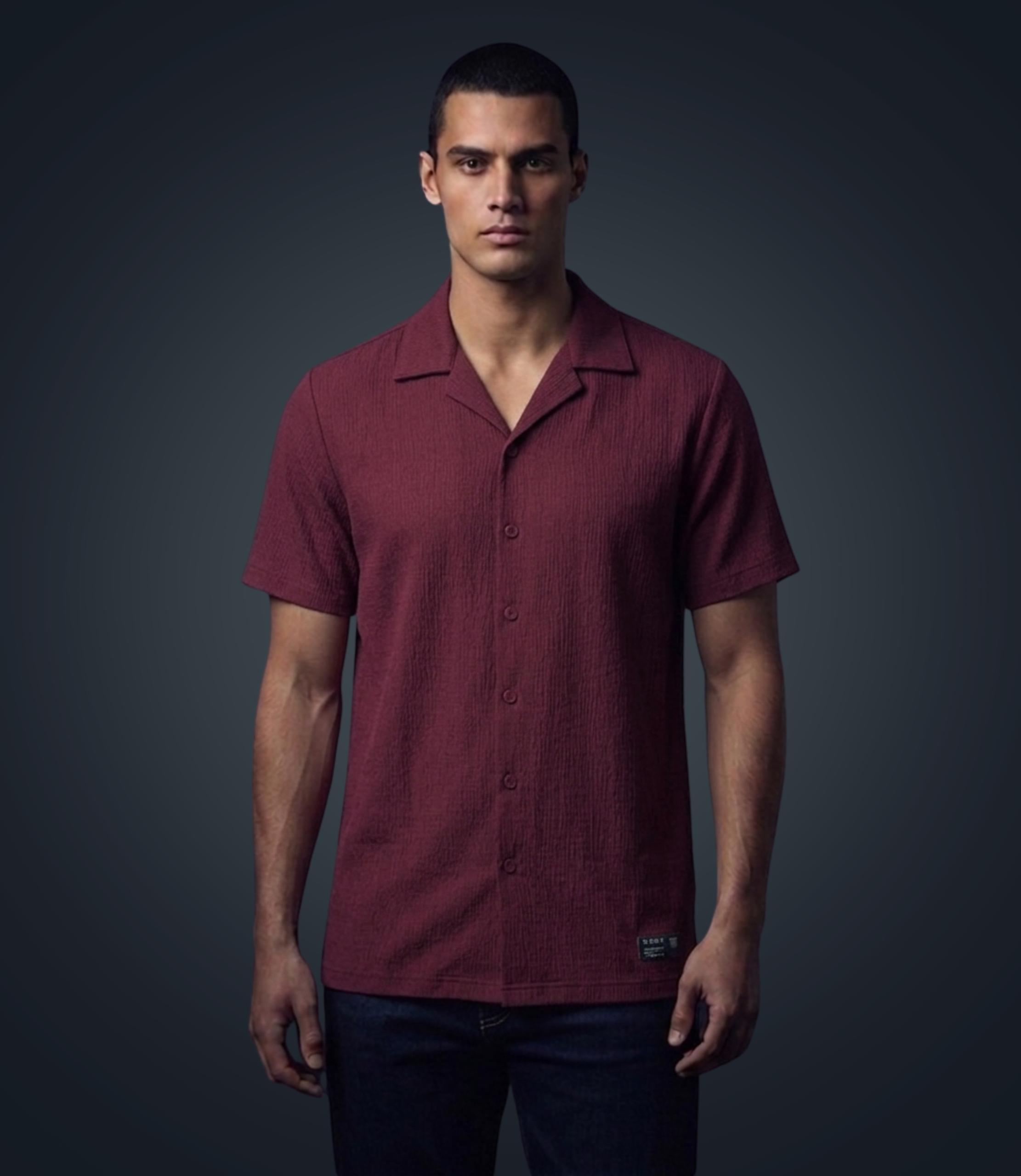 Man wearing a maroon short-sleeve shirt against a dark background