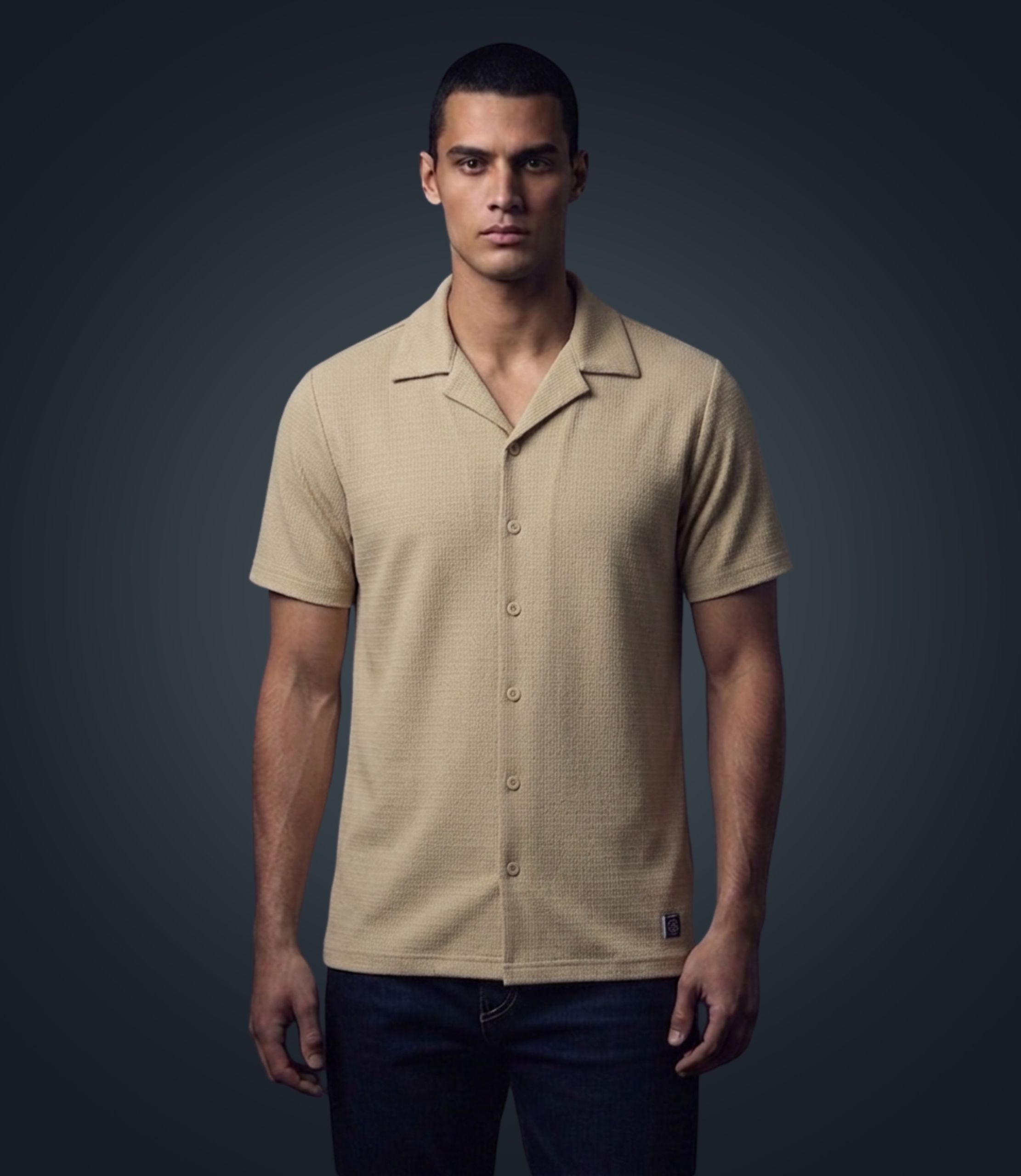 Man wearing a beige short-sleeve button-up shirt against a dark background